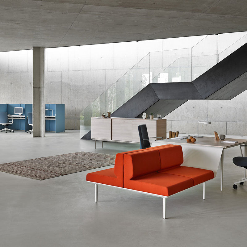 Modern office space with an orange sofa, glass walls, and concrete ceiling.